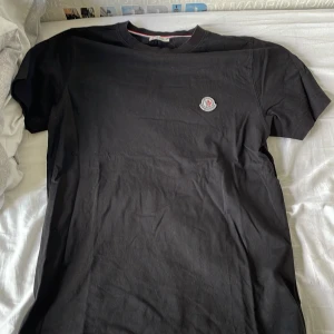 Svart T-shirt med tryck - Jag säljer en svart T-shirt med ett rundaktigt tryck vid högra sidan av bröstet, T-shirten är använd mycket men är fortfarande i bra skick. Kan göra snabb affär.