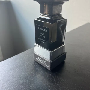Tom Ford Oud Wood Eau de Parfum 50ml - Exklusiv parfym från Tom Ford, Oud Wood Eau de Parfum i 50 ml flaska. Flaskan är svart med silverdetaljer och har en elegant, fyrkantig design. Kommer i originalförpackning med matchande svart kartong. Perfekt för dig som gillar lyxiga och unika dofter.