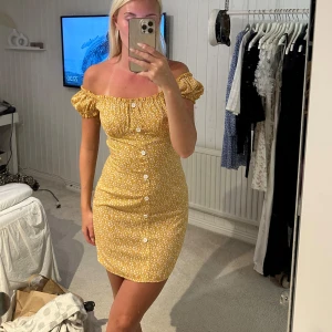 Gul blommig offshoulder kortklänning - Superfin gul kortklänning med små vita blommor, offshoulder och puffärmar.🥰
