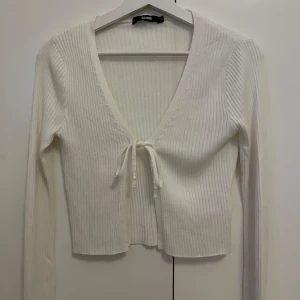 Vit ribbad omlottopp från Bik Bok - Supersnygg vit ribbad omlottopp från Bik Bok med v-ringning och knyt framtill. Långärmad och croppad modell som sitter riktigt snyggt. Perfekt att styla med jeans eller kjol för en trendig look.