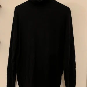 Svart polotröja i mjuk bomull - Klassisk svart polotröja med hög krage och långa ärmar. Tröjan är i mjuk  och har en stilren, enkel design som passar perfekt till lager-på-lager. Ribbad kant vid halsen ger extra detalj. Perfekt för dig som gillar minimalistisk stil.