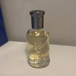 Hugo Boss Bottled parfym - Klassisk parfym från Hugo Boss i en genomskinlig glasflaska med silverfärgad metallkork. Flaskan har BOSS ingraverat vertikalt och innehåller en ljusgul vätska. Perfekt för dig som gillar stilrena och tidlösa dofter.