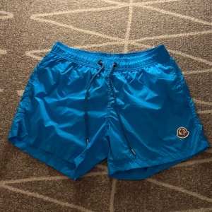 Blåa Moncler badshorts - Säljer ett par sprilans nya moncler badshorts i storlek M med den klassiska loggan på benet. Perfekt nu till sommaren. Pris kan diskuteras 