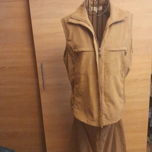 Beige sett från Cappuccini - Säljer ett beige sett från Cappuccini med dragkedja framtill och två bröstfickor med dragkedja. Settet har klassisk krage och är tillverkad i ett kraftigare bomullstyg som ger en cool och avslappnad look.