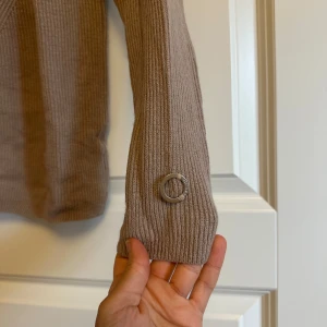 Beige ribbad stickad höst vinter tröja Stockh lm MQ - Beige ribbstickad tröja från Stockh lm med lång ärm. Tröjan har en rund hals och mönster framtill. Perfekt för lager-på-lager under kyliga dagar.