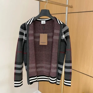 Rutig hoodie från Burberry - Snygg bomberjacka från Burberry med klassiskt rutigt mönster i svart, grått, vitt och röda detaljer. Jackan har dragkedja framtill, ribbade muddar och krage med svarta och vita ränder. Perfekt för dig som vill sticka ut med en ikonisk look.