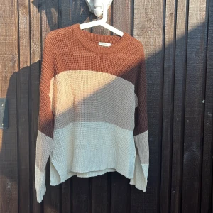 Randig stickad tröja från Stradivarius - Säljer en snygg stickad tröja från Stradivarius i storlek M. Tröjan har breda ränder i brunt, beige och vitt och är lite oversized med lång ärm och rund hals. Perfekt för lager på lager och chill höst- och vinterstil.