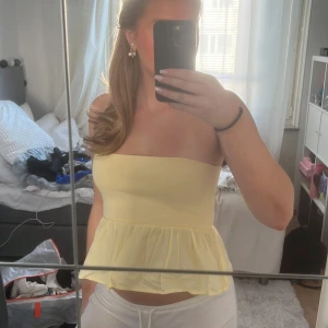Gul axelbandslös topp - Säljer en söt gul axelbandslös topp med volangdetalj. Perfekt för varma sommardagar och ger en fräsch look. Toppen är croppad och har en luftig passform.