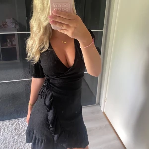 Svart omlottklänning med volang - Supersnygg svart kort omlottklänning med puffärmar och djup v-ringning. Klänningen har knyt i sidan och volangdetaljer💗💗