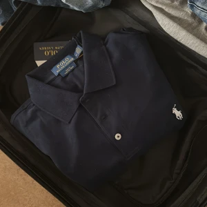 Marinblå pikétröja Polo Ralph Lauren - Snygg marinblå pikétröja från Polo Ralph Lauren i slim fit med stretch, perfekt för sommaren. Vet inte om den är äkta eller inte köpte den från vinted, men den ser väldigt äkta ut iaf, skriv vid funderingar eller prisförslag😊
