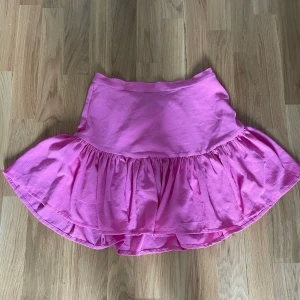 Rosa volangkjol med resårmidja - Supersöt rosa kortkjol med volangkant och resår i midjan. Kjolen har en luftig och flowy känsla, perfekt för varma dagar. Materialet känns som bomull och har en lätt struktur. Passformen är normal och kjolen är enkel att styla till olika looks.