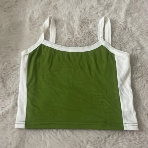 Grön och vit linnetopp - Snygg linnetopp i grönt med vita kanter och breda axelband. Toppen har en rak, croppad passform och är perfekt för varma dagar. Enkel och stilren design som passar till jeans eller kjol. Inga fläckar och en fin passform. Ingen etiket tyvärr men riktigt fin.
