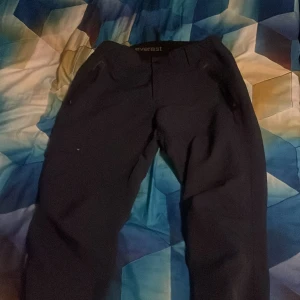 Mörk blåa  täckbyxor från Everest - Säljer ett par mörk blåa  täckbyxor från Everest. Byxorna har dragkedjor vid fickorna och är perfekta för kalla dagar. De är tillverkade i ett slitstarkt material och har en bekväm passform med normal midja.