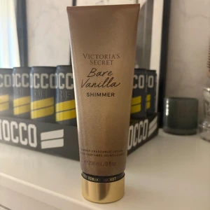 Victoria's Secret Bare Vanilla Shimmer - Glittrande bodylotion från Victoria's Secret i doften Bare Vanilla. Kommer i en lyxig guldskimrande tub på 236 ml. Ger huden en fin shimmer-effekt och en söt vaniljdoft. Perfekt för dig som vill ha extra glow till din look.