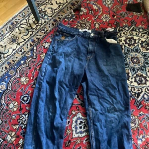 Blå jeans från Polar Skate Co 34/32 - Säljer ett par klassiska blå jeans från Polar Skate Co. i storlek 34/32. Jeansen har rak passform, fem fickor och snyggt broderad logga på myntfickan. Tillverkade i slitstarkt denim med gul kontrastsöm och tydlig etikett bak i midjan.