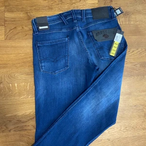 Blå Replay Anbass jeans 30/30 - Snygga blå Replay Anbass jeans med klassisk femficksdesign och tydliga detaljer som logotyp på bakfickan och läderpatch i midjan. Jeansen har en smal passform och är tillverkade i mjukt stretchigt jeansmaterial för extra komfort. Byxorna är i nytt skick. 10/10. Tveka inte på att skriva vid funderingar.