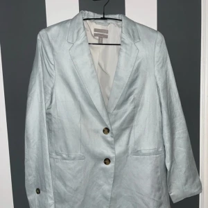 Ljusblå linnekavaj från H&M - Snygg ljusblå kavaj från H&M i linneblandning. Klassisk modell med två knappar framtill, fickor och slits bak. Perfekt för dig som gillar stilrena och fräscha looks. Passar till både jeans och kostymbyxor.Fin kavaj i linne blend  Ljusblå  Stl 36