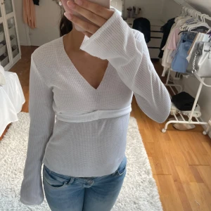 Vit topp med knytning - Superfin vit topp med v-ringning och långa ärmar. Toppen har ett strukturerat tyg och knytband i midjan som ger en snygg siluett. 