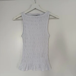 Vit smockad linnetopp från Weekday - Supersöt vit linnetopp från Weekday i smockad bomull med volangkant nertill. Ärmlös och med rund halsringning! Sitter så snyggt men kom inte till användning , endast provad!