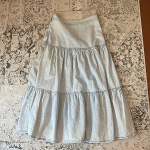 Ljusblå volangkjol från g perfect jeans - Supersöt ljusblå långkjol i jeansmaterial från g perfect jeans. Kjolen har flera volanger och en avslappnad passform som ger en chill vibe. Perfekt för dig som gillar denim och vill ha en flowy look till sommaren.