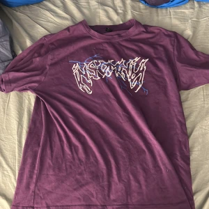 Lila t-shirt med tryck från Romwe - Cool lila t-shirt från Romwe i bomullsmix med grafiskt vitt och blått tryck framtill. Klassisk passform med rund hals och korta ärmar.