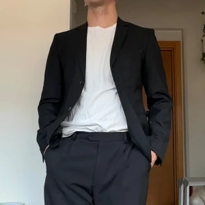 Svart kavaj Jack & Jones strl 48 - Säljer en klassisk svart kavaj från Jack & Jones Premium, storlek 48. Kavajen är skräddad med två knappar och raka slag. Perfekt för dig som vill ha en stilren och tidlös look.