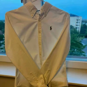 Ralph Lauren skjorta - Klassisk vit skjorta från Ralph Lauren i slim fit-modell. Skjortan har lång ärm, knappar framtill och den ikoniska broderade loggan på bröstet. Tillverkad i 100% bomull för en skön och stilren känsla.