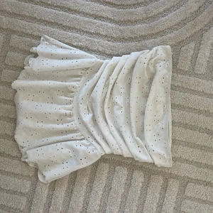 Vit topp med volang och broderi - Superfin vit topp med broderade detaljer och volangkant. Topp har en omlott-look och är perfekt för sommarens alla tillfällen. Lätt och luftig känsla, passar perfekt till en söt topp eller oversized t-shirt.