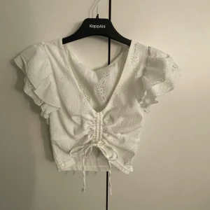 Vit blus med volang och snörning FP Sister - Superfin vit blus från FP Sister med v-ringning, volangärmar och snygg snörning framtill. Blusen har broderade detaljer och är croppad, perfekt till jeans eller kjol. Lätt och luftig, passar perfekt till sommaren.