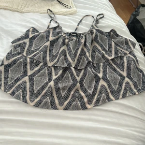 Mönstrad linnetopp med volang - Säljer en snygg linnetopp från Bik Bok med grafiskt mönster i blåa och beige/vit. Toppen har tunna axelband och en volangdetalj framtill som ger en cool och luftig känsla.