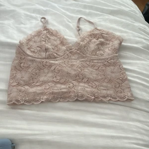 Beige spetsig linnetopp - Supersöt beige linnetopp i spets med blommigt mönster och tunna axelband. Toppen har v-ringning och fina vågiga kanter nertill.