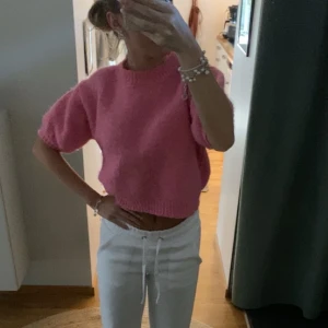Rosa stickad tröja - Superfin rosa stickad tröja med croppad passform och korta ärmar. Tröjan har en rund halsringning och ribbade muddar vid ärmslut och nederkant. Perfekt att styla med både jeans och kjol för en trendig look.