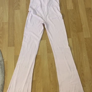 Ljusrosa yogapants från Gina Tricot - Supersnygga ljusrosa yogapants från Gina Tricot med långa ben och utsvängda byxben. Mjuk och stretchig bomullskänsla som sitter bekvämt. Perfekt för dig som gillar en chill och trendig stil. Lite missfärgat på baksidan vid fötterna av byxorna.