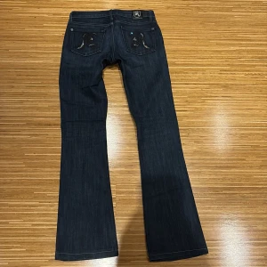 Rock & Republic mörkblå bootcut jeans - Mörkblå jeans från Rock & Republic med bootcut passform. Snygga detaljer med strass på bakfickorna som formar ett R. Klassisk femficksmodell med silverfärgade knappar och logga på bakfickan. Perfekta för dig som gillar en stilren men ändå extra look.✨💖