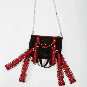 Tripp nyc Svart och röd axelväska med kedja - Unik nyc tripp svart axelväska med röda detaljer, silverfärgade nitar och kedja. Väskan har dekorativa band med svarta spetskanter och coola metalldetaljer. Perfekt för dig som gillar alternativ stil och vill sticka ut med accessoarer som har attityd.