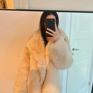 Beige fluffig pälsjacka - Supermjuk och oversized beige pälsjacka med bred krage och långa ärmar. Perfekt för dig som vill ha en statement-jacka som håller dig varm och snygg under kalla dagar. Jackan har en riktigt lyxig och trendig vibe.