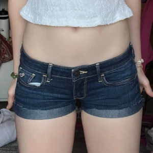 Mörkblå jeansshorts från Hollister - Snygga mörkblå jeansshorts från Hollister med låg midja och klassiska fickor både fram och bak. Shortsen har uppvikta benslut och tydliga kontrastsömmar. Perfekta för sommardagar och har en riktigt chill vibe.