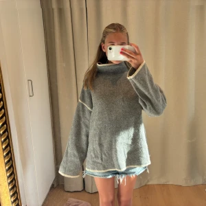 Grå oversized stickad polotröja - Mysig grå stickad polotröja med oversized passform och vida ärmar. Tröjan har ljusa kontrastsömmar vid ärmslut och nederkant samt en hög krage. Super mysig till hösten 