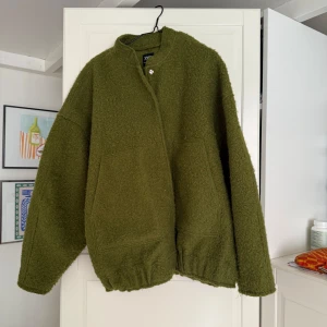 Olivgrön teddyjacka från Zara - Säljer en olivgrön teddyjacka från Zara med oversized passform. Jackan har två stora fickor framtill, ståkrage och stängs med en knapp upptill. 