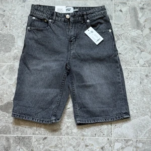Grå jeansshorts från 157, storlek 150 - Snygga grå jeansshorts från 157 i rak modell med fem klassiska fickor och bälteshällor. Shortsen har normal passform och stängs med knapp och dragkedja. Perfekta för en chill och stilren look i sommar.