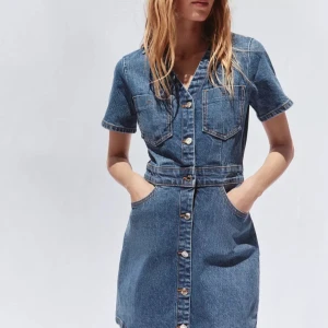 Kort jeansklänning med knappar - Snygg kort jeansklänning i blå denim med korta ärmar, knappar hela vägen framtill och flera fickor både fram och bak. Klänningen har en markerad midja och klassisk skjortkrage. Perfekt för dig som gillar en avslappnad men trendig stil. Endast använd fåtal gånger. 