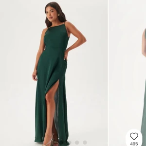 Mörkgrön lång balklänning med slits - Elegant mörkgrön långklänning med smala axelband, djup v-ringad rygg och hög slits framtill. Klänningen har en mjukt fallande siluett och stängs med dragkedja i sidan. Perfekt för dig som vill sticka ut med en stilren look.