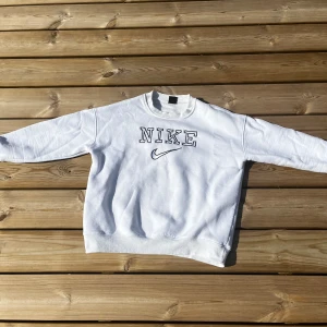 Vit Nike tröja - Säljer en clean vit sweatshirt från Nike i storlek L. Tröjan har broderad Nike-logga och text framtill, rund halsringning och långa ärmar. Perfekt för dig som gillar sportig och avslappnad stil. Materialet är mjukt och skönt, troligtvis bomullsmix.
