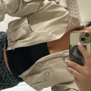 Beige bomberjacka med fickor - Snygg beige bomberjacka med dragkedja framtill och stora fickor med tryckknappar. Jackan har elastiska muddar vid ärmslut och midja för en schysst passform. Perfekt att slänga på sig över en hoodie eller crop top. Stilren och enkel att matcha.