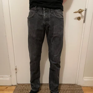 Tiger of Sweden Jeans - Säljer ett par snygga gråa Tiger of Sweden Jeans i färgen kid jet black. De är i storlek W30 L32. Jeansen är i bra skick bortsett från defekten i bild 4 och slitningen vid hälen i bild 5. Jag säljer nu dessa för endast 99kr. Hör av er vid frågor eller funderingar.