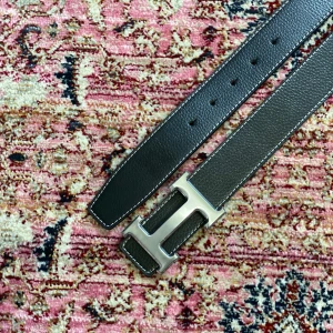 Svart H bälte - Snyggt svart 110cm bälte med klassiskt silverfärgat H-spänne. Bältet har vit kontrastsöm längs kanterna och en stilren, rak form. Perfekt accessoar för att lyfta vilken outfit som helst.