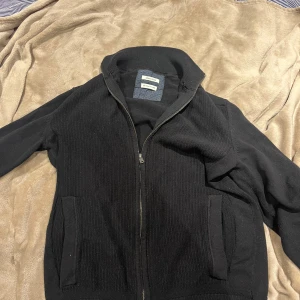 Svart stickad tröja från Tom Tailor - Svart stickad tröja från Tom Tailor i ekologisk bomull. Tröjan har dragkedja framtill, ribbade muddar och två fickor på sidorna. Perfekt för dig som gillar en clean och enkel stil med lite edge. Finns tecken på användning men absolut ingenting man tänker på. inga defekter pris 250