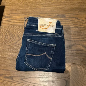 Mörkblå jeans från Jacob Cohën, stl 28 - Snygga mörkblå jeans från Jacob Cohën i klassisk femficksmodell. Jeansen har kontrastsömmar, patch med logga bak och coolt broderat citat på insidan. Tillverkade i mjukt denimtyg som sitter skönt hela dagen.