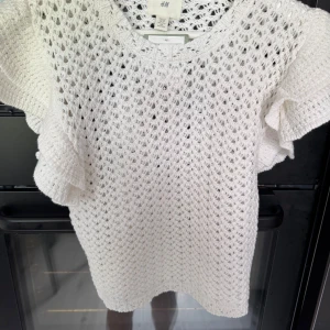 Vit stickad topp med volangärm H&M - Superfin vit stickad topp från H&M med korta volangärmar och luftig virkad känsla. Perfekt för vår och sommar, lätt att styla med jeans eller kjol. Rund halsringning och snygg struktur som ger en trendig look.