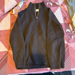 Svart stickad tröja med half zip - Svart stickad tröja från Gant med ribbade muddar och krage. Tröjan har en snygg half zip-dragkedja vid halsen som ger en sportig och stilren look. Perfekt för lager-på-lager och funkar året runt när du vill vara både chill och snygg.